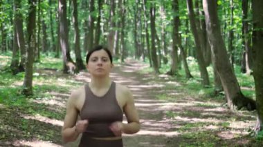 Çekici, sportif bir kadın yaz parkında dışarı çıkıp nabzını kontrol ediyor, akıllı saatini kontrol ediyor. Kadın sabah ormanında koşuyor. Sağlıklı yaşam tarzı kavramı