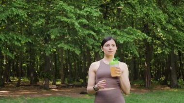Atletik kadın bcaa amino asitlerle spor besinleri içiyor ve Shaker 'dan vitaminler alıyor, yaz parkında sabah antrenmanı, yavaş çekim yörünge hareketi, sağlıklı yaşam tarzı konsepti.