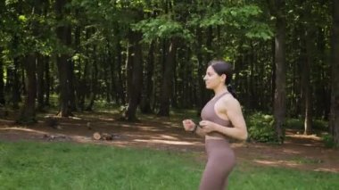 Bir yaz parkında dışarı koşan çekici bir kadının yan görüntüsü, sabah ormanda koşan bir kadın, ağır çekim. Sağlıklı yaşam tarzı kavramı