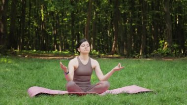 Çekici sporcu kadın yoga minderinde lotus pozisyonunda oturuyor ve yaz parkında meditasyon yapıyor, sağlıklı yaşam tarzı konsepti.