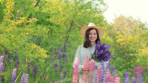 Uśmiechnięta Atrakcyjna Młoda Kobieta Sukience Kapeluszu Bukietem Kwiatów Łubinu Spacerująca — Wideo stockowe