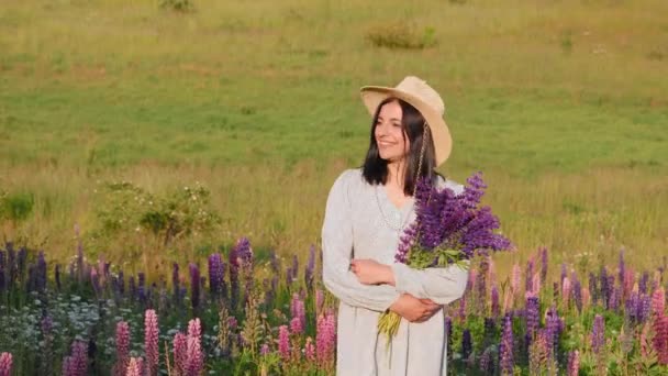 Uśmiechnięta Atrakcyjna Młoda Kobieta Sukience Kapeluszu Bukietem Kwiatów Łubinu Spacerująca — Wideo stockowe