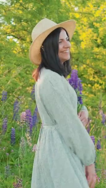 Uśmiechnięta Atrakcyjna Młoda Kobieta Sukience Kapeluszu Trzymająca Bukiet Kwiatów Łubinu — Wideo stockowe