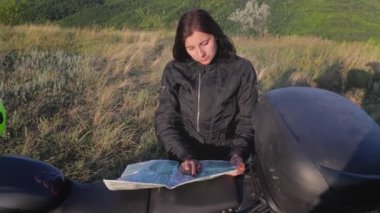 Kadın gezgin ve motosikletçi bir nehir ve yüksek kanyonda kamp yapmak için durdu ve kağıt haritada yeni yerler, manzaralı doğa manzarası