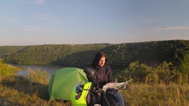 Kadın gezgin ve motosikletçi bir nehir ve yüksek kanyonda kamp yapmak için durdu ve kağıt haritada yeni yerler, manzaralı doğa manzarası