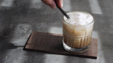Bir bardakta buzlu latte, espresso ve buz ile çırpılmış süt karıştıran pipetli bir erkek el.