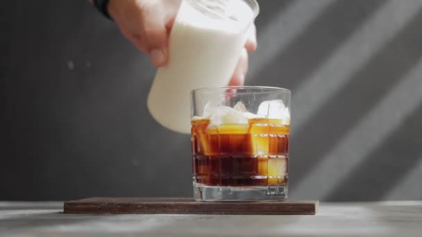 男性の手はエスプレッソコーヒーとアイスキューブとガラスにホイップミルクを注ぐ 冷たいアイスラテコーヒーを作るプロセス — ストック動画