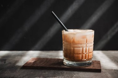 Koyu arka planda pipetle bardakta buzlu latte kahve, yaz içeceği..