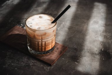 Koyu arka planda pipetle bardakta buzlu latte kahve, yaz içeceği..