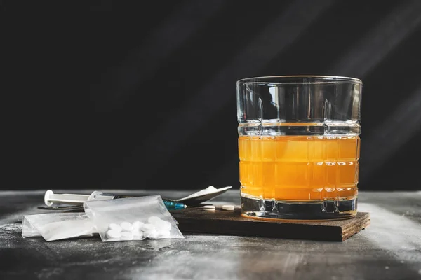 stock image Alcohol drink in a glass, syringe with a dose of drugs, white pills and narcotics powder in a transparent bag on dark background. Concept of addiction, abuse and bad habits.