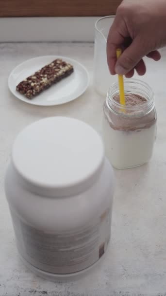 ミルクとガラス瓶にホエイプロテインパウダーを混ぜたストローハンド タンパク質飲料を滑らかにするプロセス スポーツ栄養 垂直ビデオ — ストック動画