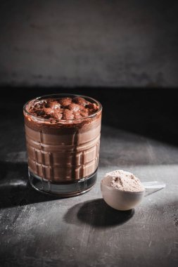 Bir bardak sağlıklı çikolatalı milkshake, koyu arkaplanda protein tozu..