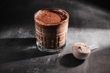 Bir bardak sağlıklı çikolatalı milkshake, koyu arkaplanda protein tozu..