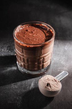 Bir bardak sağlıklı çikolatalı milkshake, koyu arkaplanda protein tozu..