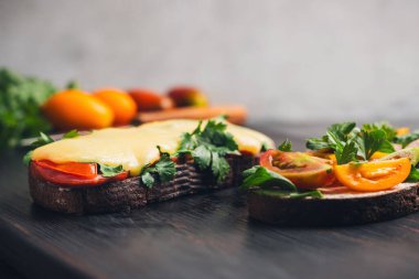 Kızarmış ekmekli iki sandviç, roka, maydanoz ve domates ve erimiş peynir ve pastırma..