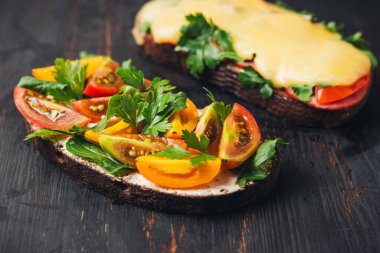 Kızarmış ekmekli iki sandviç, roka, maydanoz ve domates ve erimiş peynir ve pastırma..