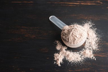 Plastik bir kaşık içindeki beyaz çikolatalı protein tozu koyu ahşap arka planda..