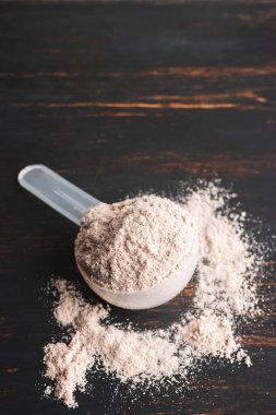 Plastik bir kaşık içindeki beyaz çikolatalı protein tozu koyu ahşap arka planda..