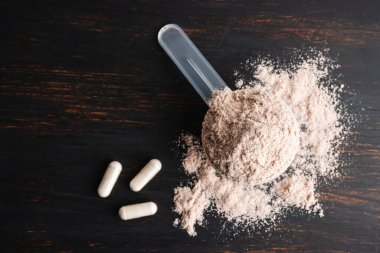Bir kepçe çikolatalı süt proteini izole edilmiş beyaz amino asit ve kreatin kapsülleri koyu ahşap bir tahtada vücut geliştiren gıda takviyeleri..
