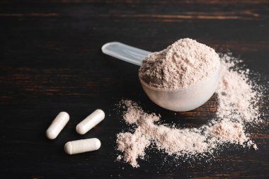 Bir kepçe çikolatalı süt proteini izole, beyaz amino asit ve kreatin kapsülleri, kara tahta üzerinde vücut geliştiren gıda takviyeleri..