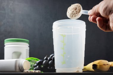 Erkek eli süt tozu kepçesinin içine soya proteini tozu koyar. Beyaz amino asit, vitamin, protein çikolatası ve muz kapsülleri. Koyu bir tahta üzerinde, vücut geliştiren gıda takviyeleri.