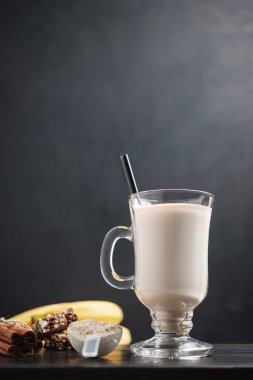 Bir bardak protein milkshake, saman ve bir kepçe beyaz protein tozu beyaz amino asit kapsülleri, vitaminler, protein barı ve muzlar koyu ahşap bir tahtanın üzerinde, vücut geliştiren gıda takviyeleri..