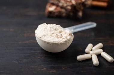 Bir kepçe whey veya soya protein tozu, beyaz amino asit kapsülleri, vitaminler, kreatin, protein çikolatası, vücut geliştirme gıdaları, koyu ahşap bir tahtanın üzerindeki spor gıdaları..