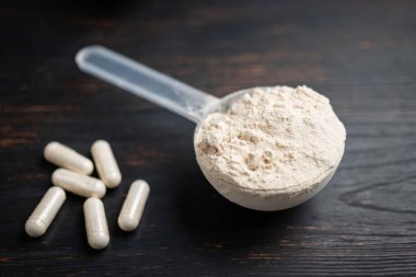 Süt veya soya proteini tozu, beyaz amino asit kapsülleri, vitaminler ve kreatin, vücut geliştiren gıda takviyeleri, siyah ahşap bir tahtanın üzerindeki spor besinleri..
