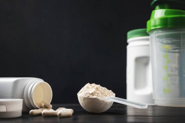 Süt veya soya proteini tozu, beyaz amino asit kapsülleri, vitaminler ve kreatin, vücut geliştiren gıda takviyeleri, spor beslenmesi, siyah tahta üzerinde plastik karıştırıcı..
