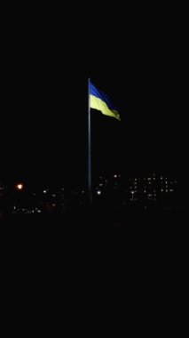 Gece kentinde bayrak direğinde mavi ve sarı renkli büyük Ukrayna bayrağı, dikey 4k