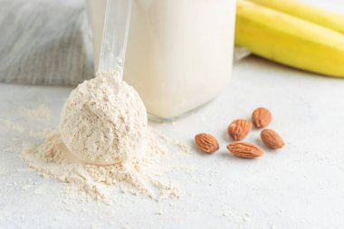 Beyaz arka planda beyaz protein tozu, cam kavanoz protein milkshake içeceği veya smoothie, muz ve badem fıstığı. Spor beslenmesi, vücut geliştirme gıda takviyeleri..