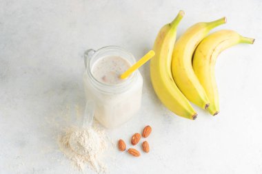 Cam kavanoz protein milkshake ya da smoothie ve beyaz arka planda kaşık, muz ve badem fıstığı içinde beyaz protein tozu. Spor beslenmesi, vücut geliştirme gıda takviyeleri..