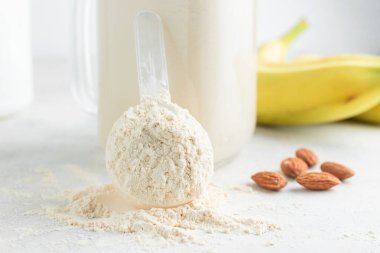 Beyaz arka planda beyaz protein tozu, cam kavanoz protein milkshake içeceği veya smoothie, muz ve badem fıstığı. Spor beslenmesi, vücut geliştirme gıda takviyeleri..