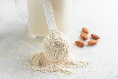 Ölçme kaşığında beyaz protein tozu, beyaz arka planda bir kavanoz protein milkshake ya da smoothie, badem fıstığı. Spor beslenmesi, vücut geliştirme gıda takviyeleri..