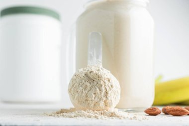 Beyaz arka planda beyaz protein tozu, cam kavanoz protein milkshake içeceği veya smoothie, muz ve badem fıstığı. Spor beslenmesi, vücut geliştirme gıda takviyeleri..