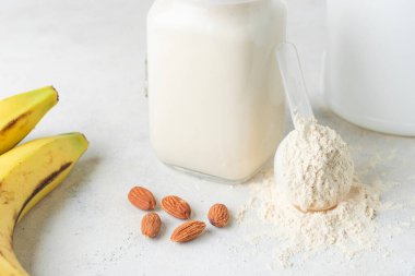Beyaz arka planda beyaz protein tozu, cam kavanoz protein milkshake içeceği veya smoothie, muz ve badem fıstığı. Spor beslenmesi, vücut geliştirme gıda takviyeleri..