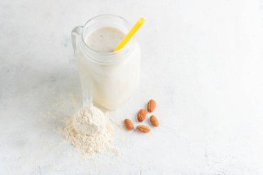 Cam kavanoz protein milkshake ya da smoothie ve beyaz arka planda badem fıstığı ölçme kaşığında beyaz protein tozu. Spor beslenmesi, vücut geliştirme gıda takviyeleri..