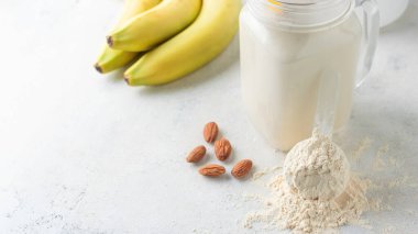 Beyaz arka planda beyaz protein tozu, cam kavanoz protein milkshake içeceği veya smoothie, muz ve badem fıstığı. Spor beslenmesi, vücut geliştirme gıda takviyeleri..