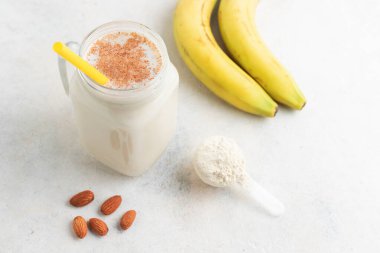 Cam kavanoz protein milkshake ya da smoothie ve beyaz arka planda kaşık, muz ve badem fıstığı içinde beyaz protein tozu. Spor beslenmesi, vücut geliştirme gıda takviyeleri..