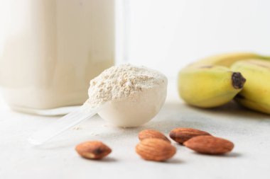 Beyaz arka planda beyaz protein tozu, cam kavanoz protein milkshake içeceği veya smoothie, muz ve badem fıstığı. Spor beslenmesi, vücut geliştirme gıda takviyeleri..