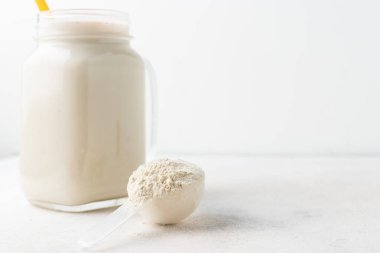 Beyaz arka planda kaşık ve cam kavanoz protein milkshake veya smoothie karışımında beyaz protein tozu. Spor beslenmesi, vücut geliştirme gıda takviyeleri..