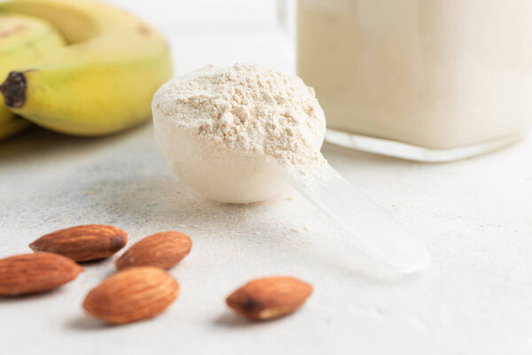 Whey protein powder in measuring spoon, glass jar of protein milkshake drink or smoothie, bananas and almond nuts on a white background. sport nutrition, bodybuilding food supplements.
