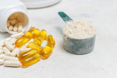 Beyaz kaşıkta beyaz protein tozu, beyaz amino asit kapsülleri, vitaminler ve sarı kapsüller beyaz arka planda Omega 3, sağlıklı beslenme ve vücut geliştirme besinleri..