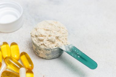 Beyaz kaşıkta beyaz protein tozu, beyaz amino asit kapsülleri, vitaminler ve sarı kapsüller beyaz arka planda Omega 3, sağlıklı beslenme ve vücut geliştirme besinleri..