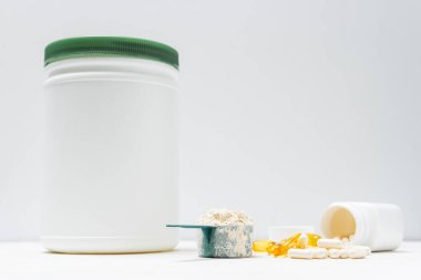 Beyaz kaşıkta beyaz protein tozu, beyaz amino asit kapsülleri, vitaminler ve sarı kapsüller beyaz arka planda Omega 3, sağlıklı beslenme ve vücut geliştirme besinleri..