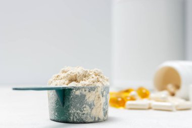 Beyaz kaşıkta beyaz protein tozu, beyaz amino asit kapsülleri, vitaminler ve sarı kapsüller beyaz arka planda Omega 3, sağlıklı beslenme ve vücut geliştirme besinleri..