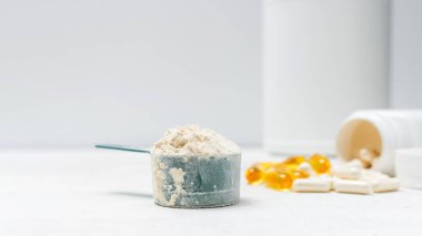 Beyaz kaşıkta beyaz protein tozu, beyaz amino asit kapsülleri, vitaminler ve sarı kapsüller beyaz arka planda Omega 3, sağlıklı beslenme ve vücut geliştirme besinleri..