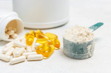Beyaz kaşıkta beyaz protein tozu, beyaz amino asit kapsülleri, vitaminler ve sarı kapsüller beyaz arka planda Omega 3, sağlıklı beslenme ve vücut geliştirme besinleri..