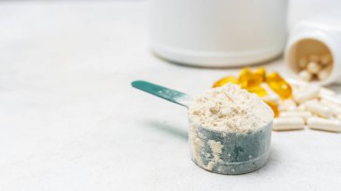 Beyaz kaşıkta beyaz protein tozu, beyaz amino asit kapsülleri, vitaminler ve sarı kapsüller beyaz arka planda Omega 3, sağlıklı beslenme ve vücut geliştirme besinleri..