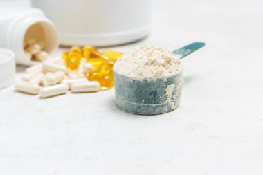 Beyaz kaşıkta beyaz protein tozu, beyaz amino asit kapsülleri, vitaminler ve sarı kapsüller beyaz arka planda Omega 3, sağlıklı beslenme ve vücut geliştirme besinleri..